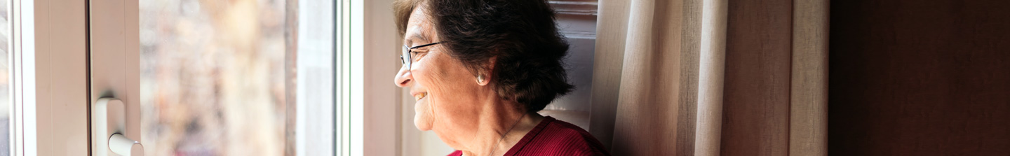 An elderly woman looking out her front door, smiling